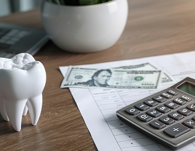 Dollar bills next to model tooth and calculator on desk