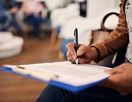 Patient’s hands filling out form on blue clipboard